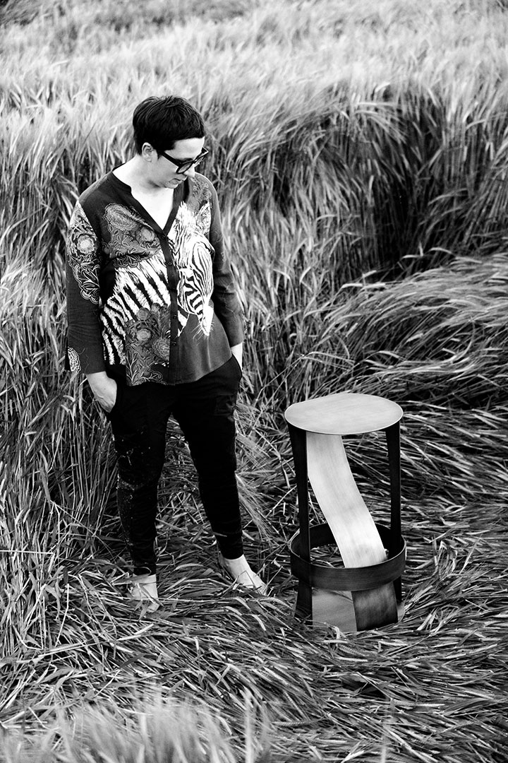 La designer Elena Rogna accanto al prototipo di uno sgabello progettato da lei, fotografata in un campo di grano.